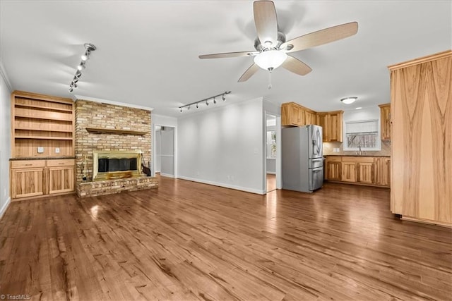 unfurnished living room featuring crown molding, ceiling fan, hardwood / wood-style floors, a fireplace, and built in shelves