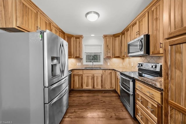 kitchen with appliances with stainless steel finishes, dark hardwood / wood-style floors, tasteful backsplash, sink, and dark stone countertops