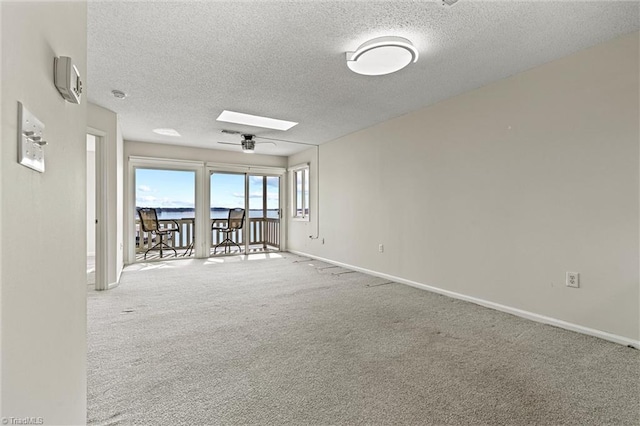 carpeted spare room featuring baseboards, a textured ceiling, and a skylight