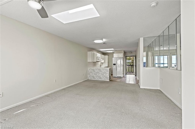 unfurnished living room with light carpet, a textured ceiling, a skylight, and baseboards