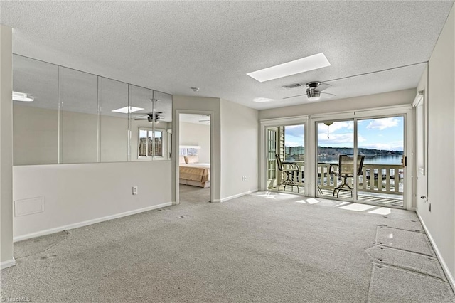 unfurnished room with carpet flooring, a textured ceiling, a skylight, and a ceiling fan