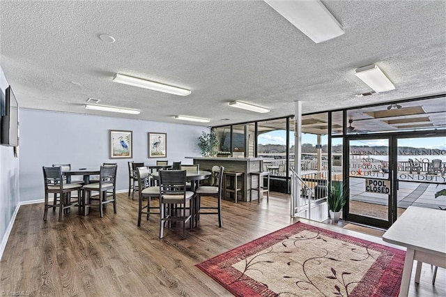 dining room with a wall of windows, wood finished floors, baseboards, and a textured ceiling