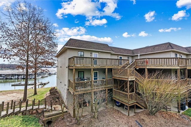 rear view of house featuring stairway, a deck with water view, and roof with shingles