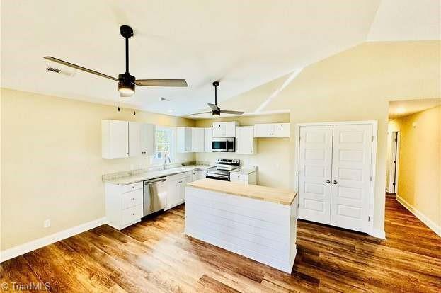 kitchen featuring stainless steel appliances, lofted ceiling, white cabinets, and dark wood-type flooring