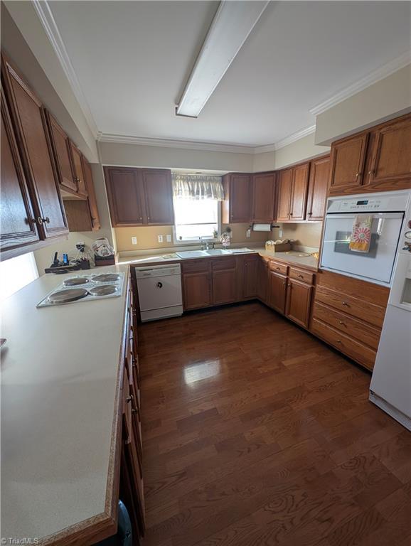 kitchen with sink, white appliances, crown molding, and dark hardwood / wood-style flooring