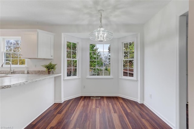 unfurnished dining area featuring dark wood-type flooring, sink, and a notable chandelier