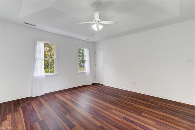 empty room featuring dark hardwood / wood-style floors, ceiling fan, and a tray ceiling