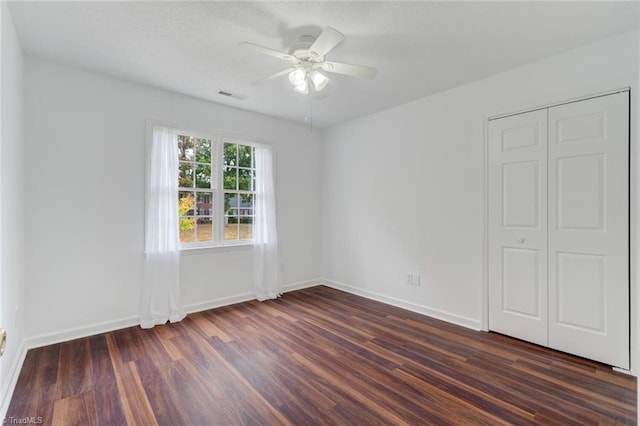 unfurnished bedroom featuring dark wood-type flooring, a closet, and ceiling fan