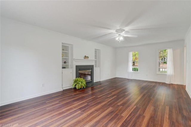 unfurnished living room featuring ornamental molding, built in features, dark wood-type flooring, and ceiling fan