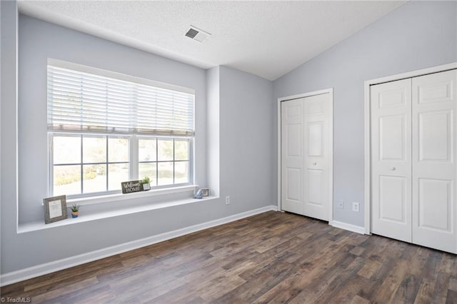 unfurnished bedroom with dark wood-type flooring, a textured ceiling, vaulted ceiling, and multiple closets