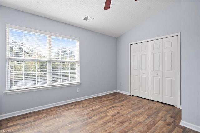 unfurnished bedroom featuring dark hardwood / wood-style flooring, vaulted ceiling, a textured ceiling, ceiling fan, and a closet