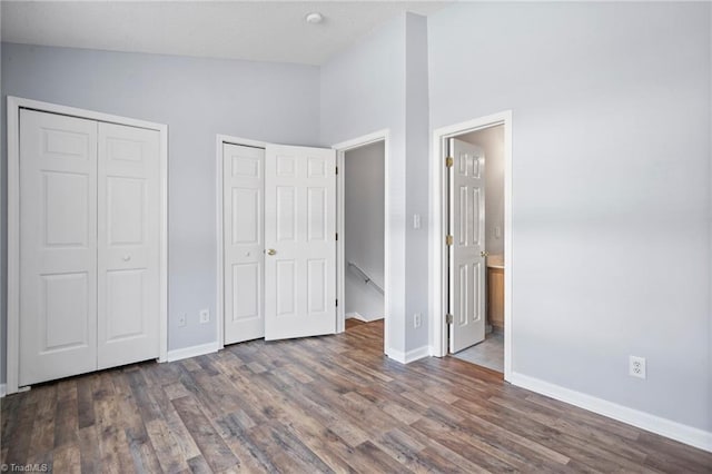 unfurnished bedroom featuring multiple closets, high vaulted ceiling, dark hardwood / wood-style floors, and ensuite bath