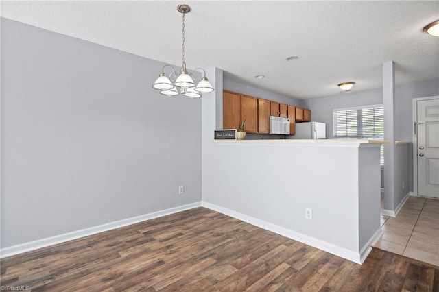 kitchen with dark wood-type flooring, an inviting chandelier, kitchen peninsula, hanging light fixtures, and white appliances