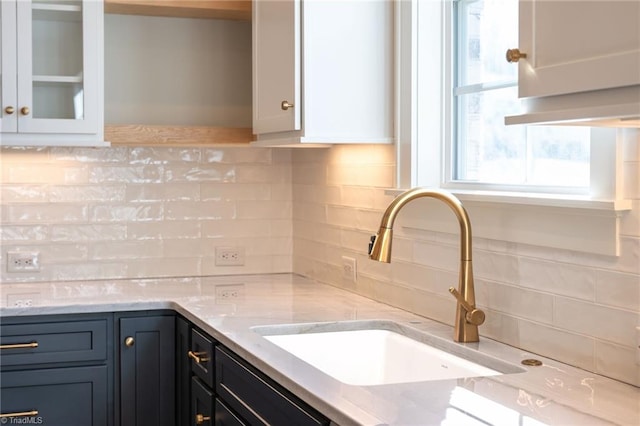 kitchen with tasteful backsplash, light stone countertops, sink, and white cabinets