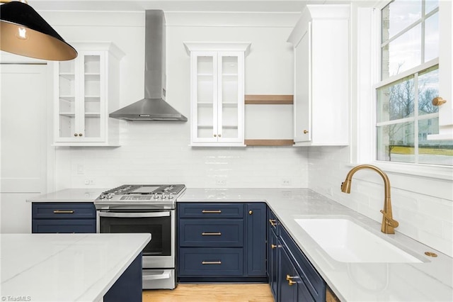 kitchen featuring blue cabinets, white cabinetry, sink, gas range, and wall chimney range hood