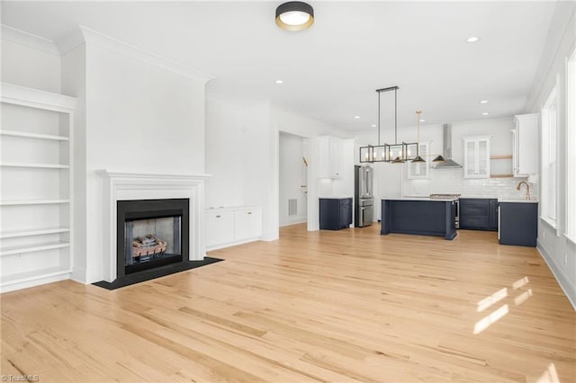 unfurnished living room featuring sink, crown molding, light hardwood / wood-style flooring, and built in features