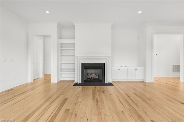 unfurnished living room featuring built in shelves, ornamental molding, and light wood-type flooring