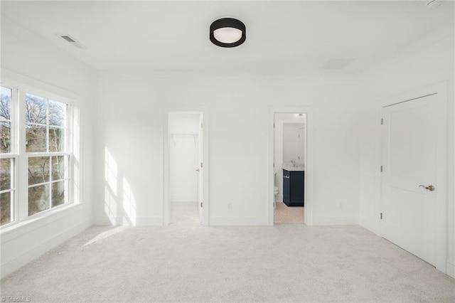 unfurnished bedroom featuring a spacious closet, light colored carpet, crown molding, ensuite bath, and a closet