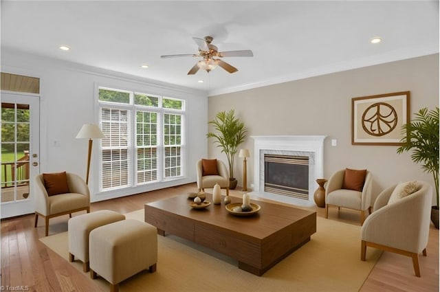living room featuring ceiling fan, light wood-style flooring, crown molding, a premium fireplace, and recessed lighting