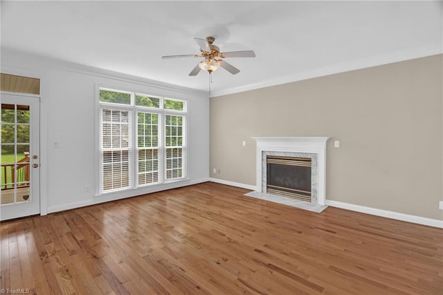 unfurnished living room featuring hardwood / wood-style flooring, a ceiling fan, crown molding, baseboards, and a premium fireplace