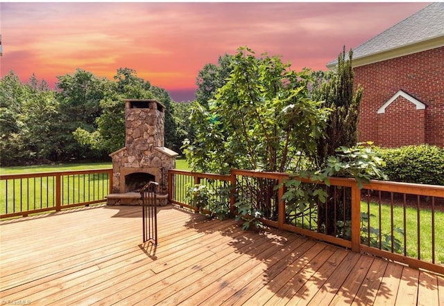 wooden terrace with an outdoor stone fireplace and a lawn