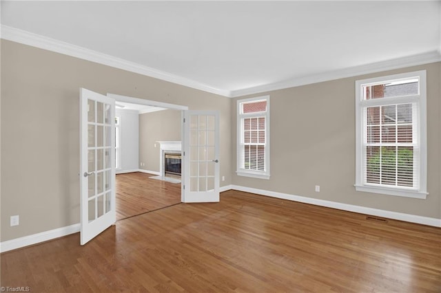 empty room with ornamental molding, baseboards, wood finished floors, and a fireplace with flush hearth