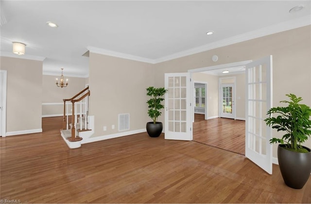 spare room with french doors, ornamental molding, wood finished floors, baseboards, and a chandelier