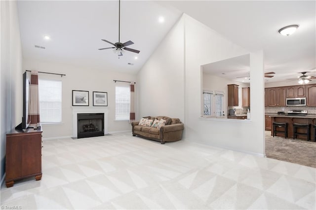 living area featuring visible vents, light colored carpet, a fireplace with flush hearth, high vaulted ceiling, and recessed lighting