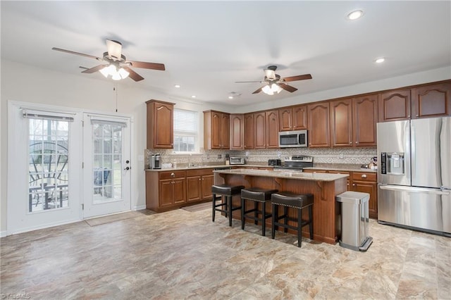 kitchen featuring tasteful backsplash, a kitchen island, brown cabinets, stainless steel appliances, and a kitchen bar