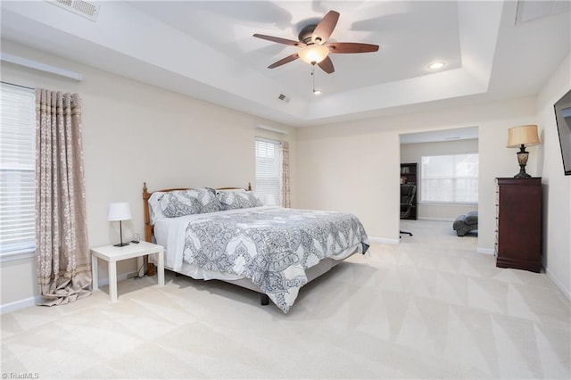 bedroom featuring light carpet, a tray ceiling, multiple windows, and baseboards