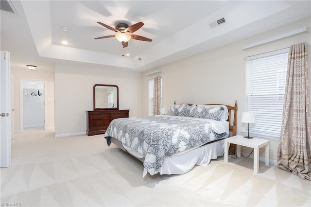 bedroom with light colored carpet, a raised ceiling, visible vents, and baseboards