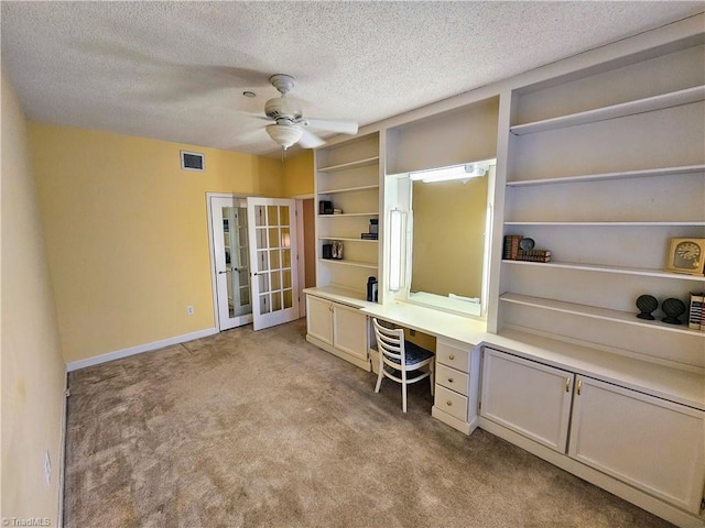 office area with built in desk, ceiling fan, a textured ceiling, and light carpet