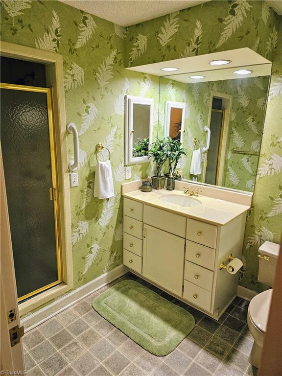 bathroom with a shower with shower door, vanity, toilet, and tile patterned floors