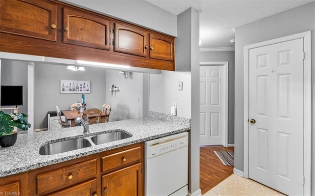 kitchen with sink, ornamental molding, light stone counters, white dishwasher, and a textured ceiling