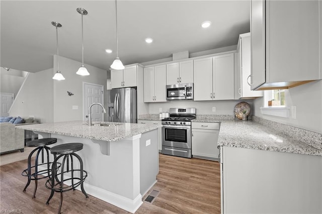 kitchen featuring open floor plan, stainless steel appliances, light wood finished floors, a kitchen bar, and white cabinetry