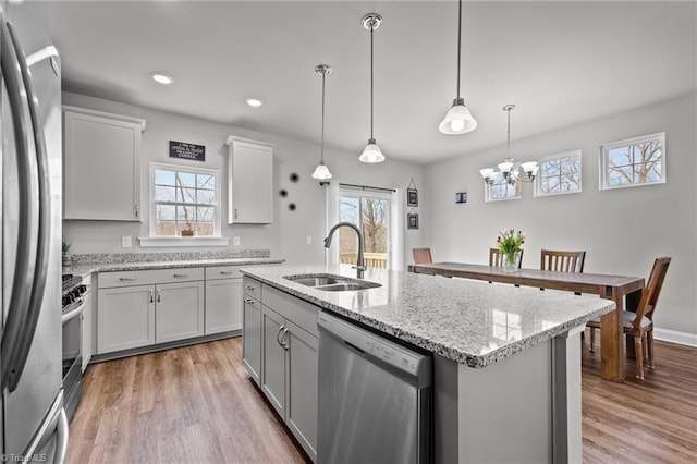 kitchen featuring stainless steel appliances, light wood-style flooring, a sink, and an island with sink