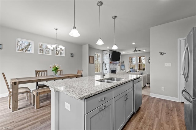 kitchen with a sink, light wood-style floors, a center island with sink, gray cabinetry, and appliances with stainless steel finishes