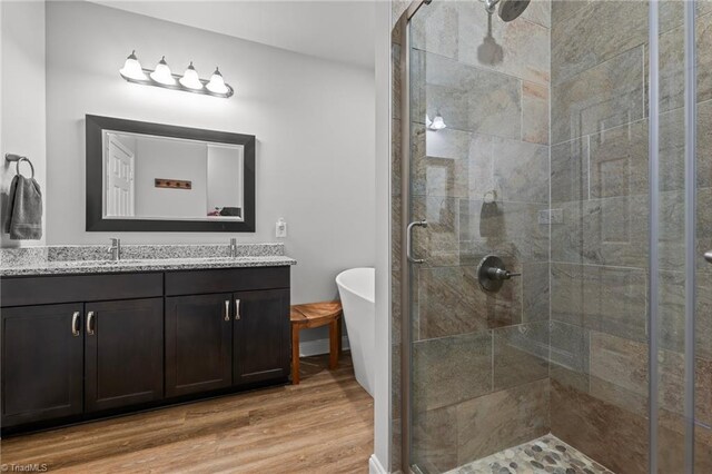 bathroom with a shower stall, a freestanding bath, wood finished floors, and double vanity