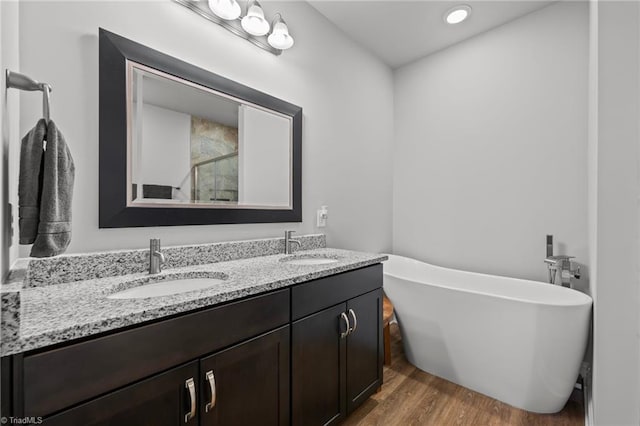 bathroom with a freestanding bath, wood finished floors, a sink, and double vanity
