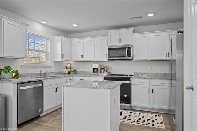 kitchen with sink, white cabinetry, a center island, appliances with stainless steel finishes, and light stone countertops