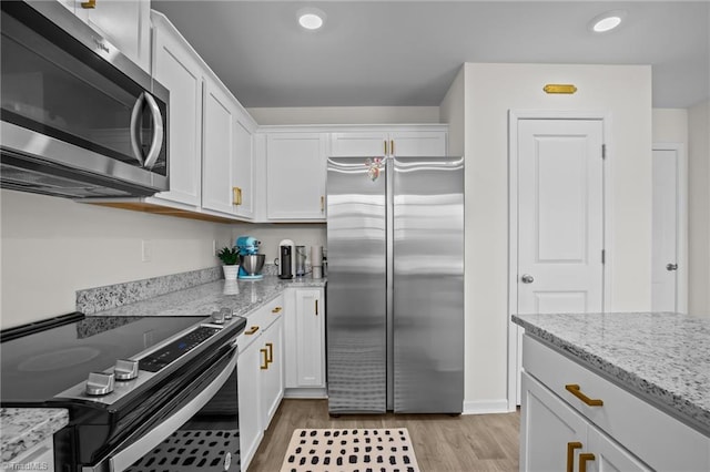 kitchen featuring light hardwood / wood-style flooring, light stone countertops, white cabinets, and appliances with stainless steel finishes