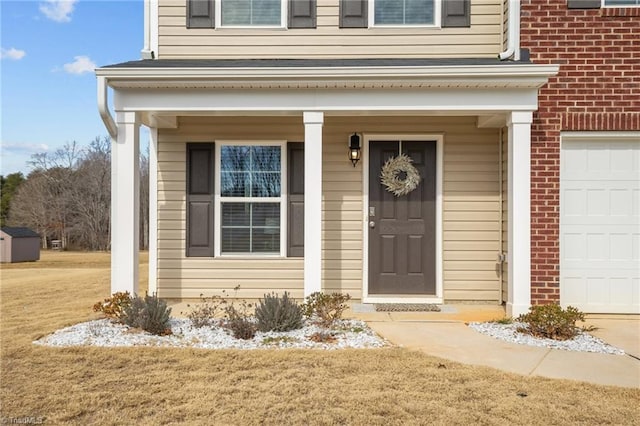 view of exterior entry featuring a garage, covered porch, and a lawn