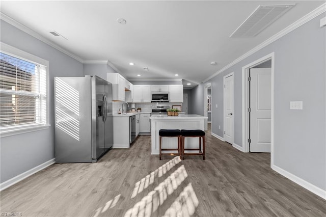 kitchen featuring stainless steel appliances, sink, white cabinetry, a kitchen bar, and a kitchen island