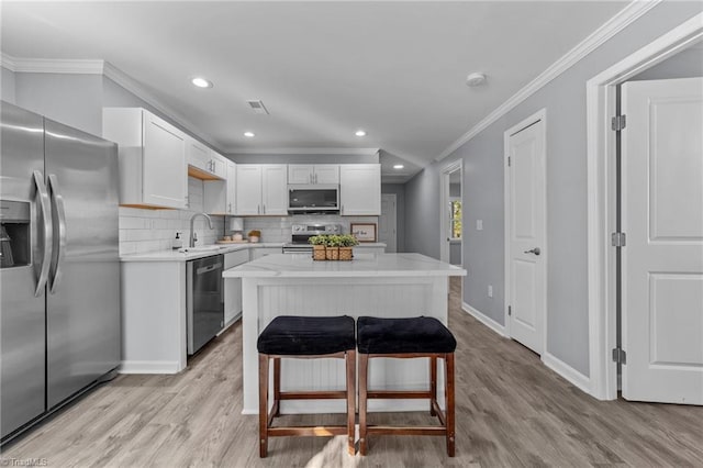 kitchen featuring stainless steel appliances, white cabinets, a center island, backsplash, and crown molding