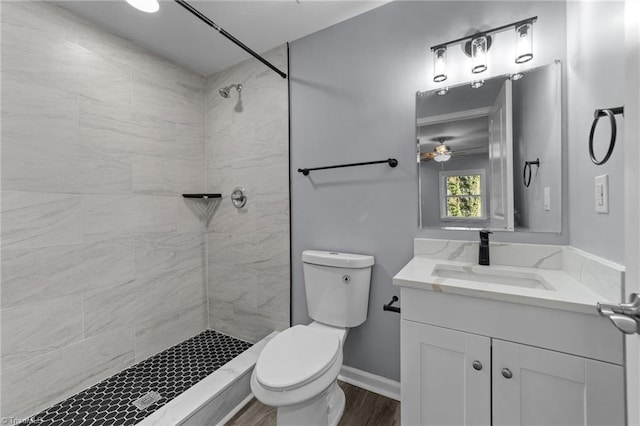 bathroom with toilet, ceiling fan, tiled shower, and vanity