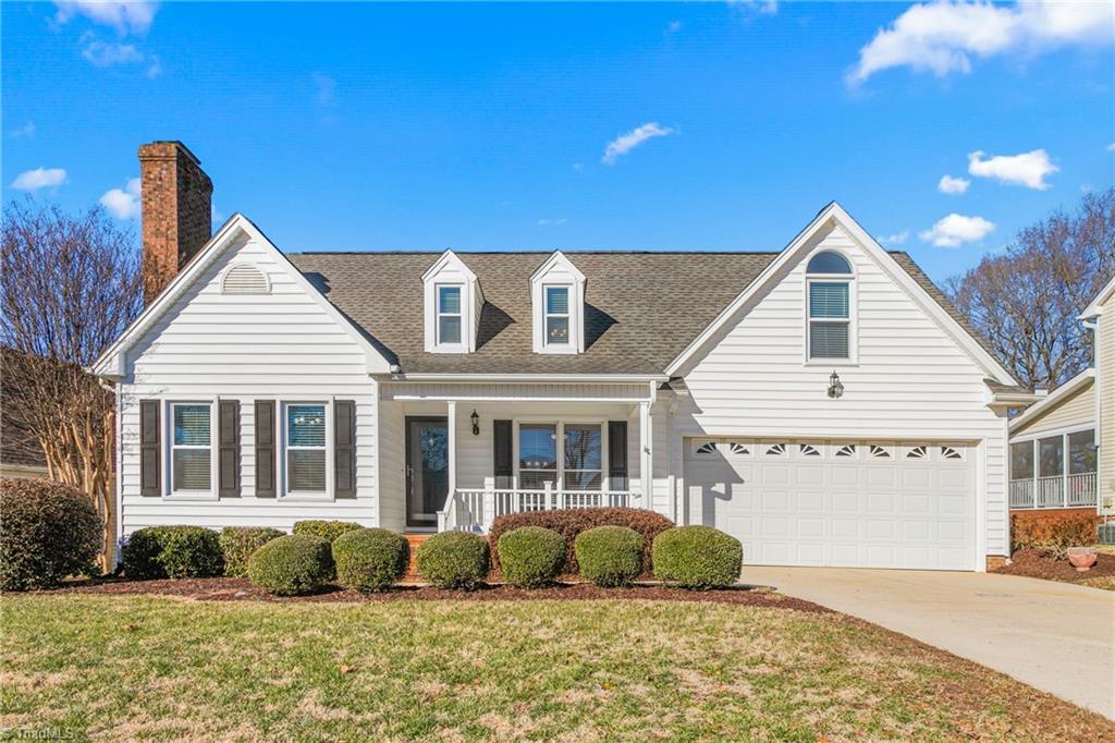 cape cod home with covered porch, a front lawn, and a garage