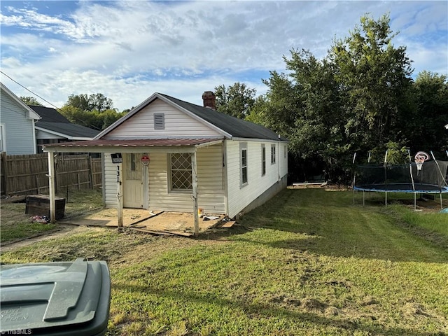 rear view of property featuring a trampoline and a yard