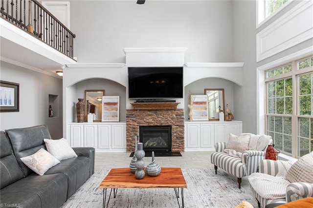 living room featuring crown molding, a towering ceiling, light hardwood / wood-style flooring, and a stone fireplace