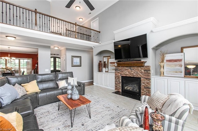 living room featuring ceiling fan with notable chandelier, ornamental molding, a towering ceiling, and a stone fireplace