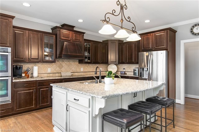 kitchen featuring crown molding, a center island with sink, dark brown cabinets, and custom exhaust hood